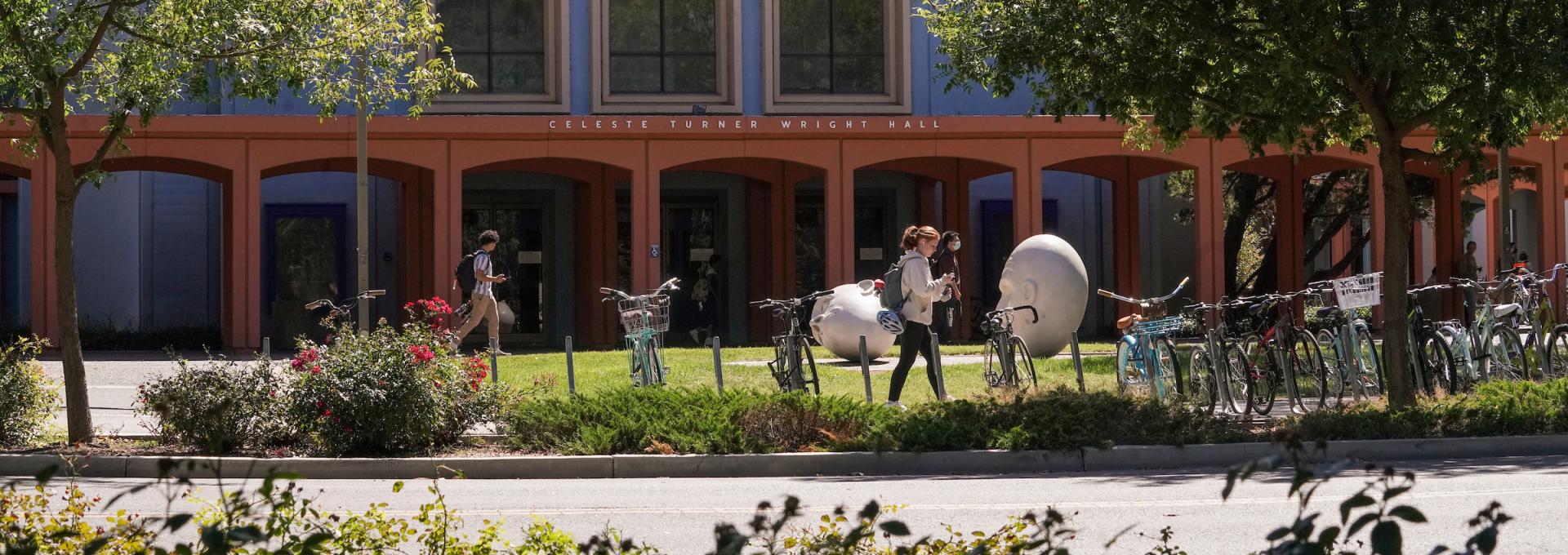 Student walking in front of a building and two egghead sculptures